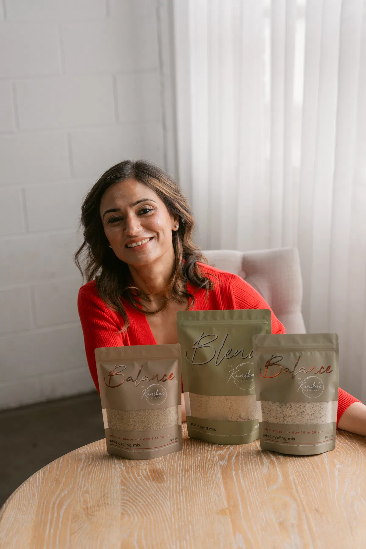 A founder smiles at a wooden table behind three pouches of her seed and nut mixes.